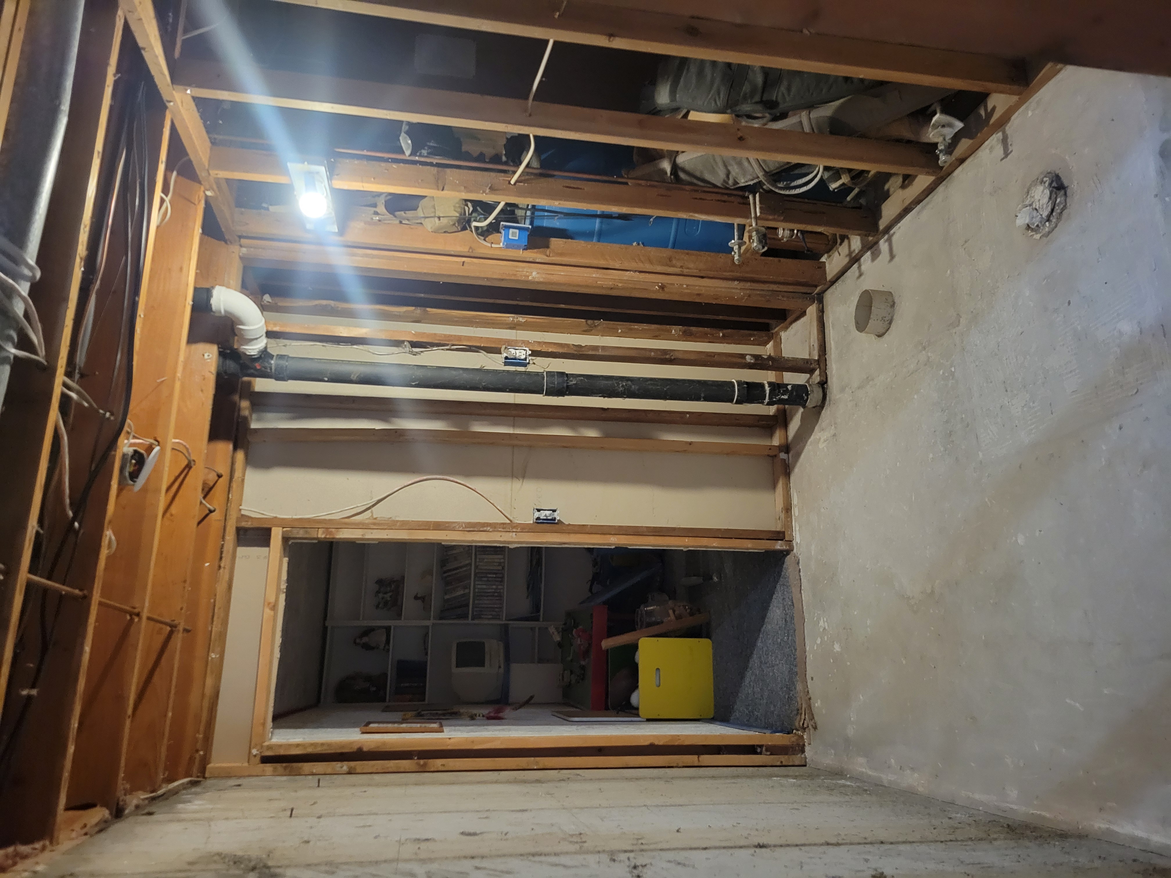 Exposed ceiling joists and plumbing pipes with dehumidifier running during mold remediation
