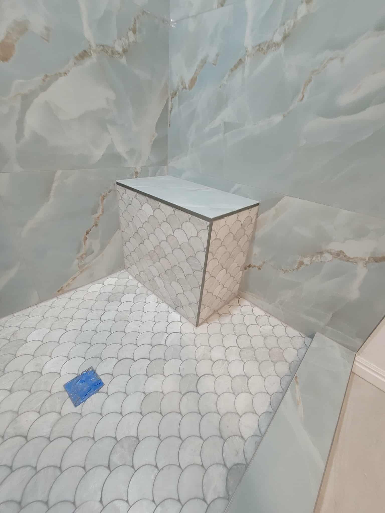 Close-up of fish scale mosaic tile on shower bench and floor with blue marble walls